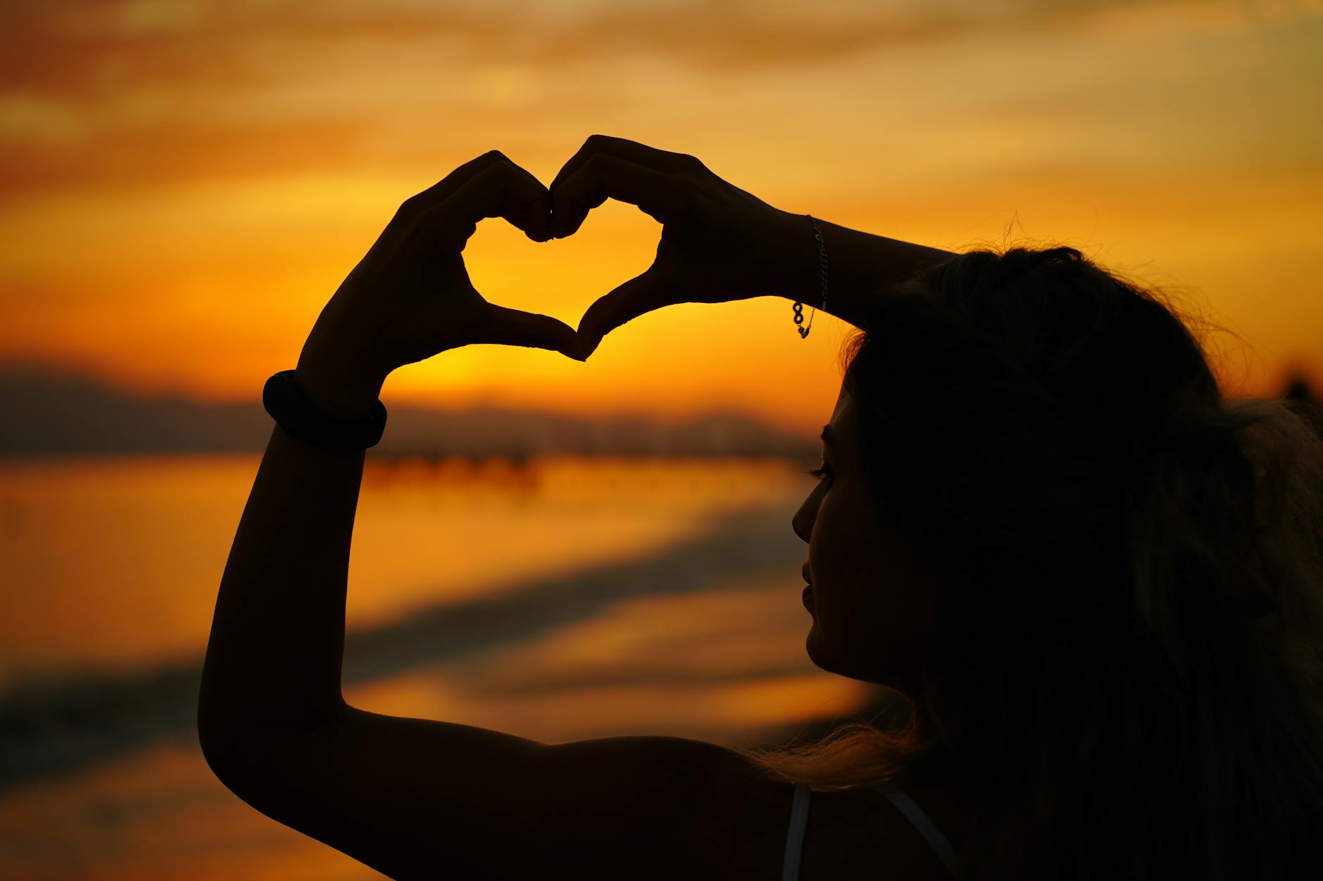 silhouette of woman making heart shape at sunset